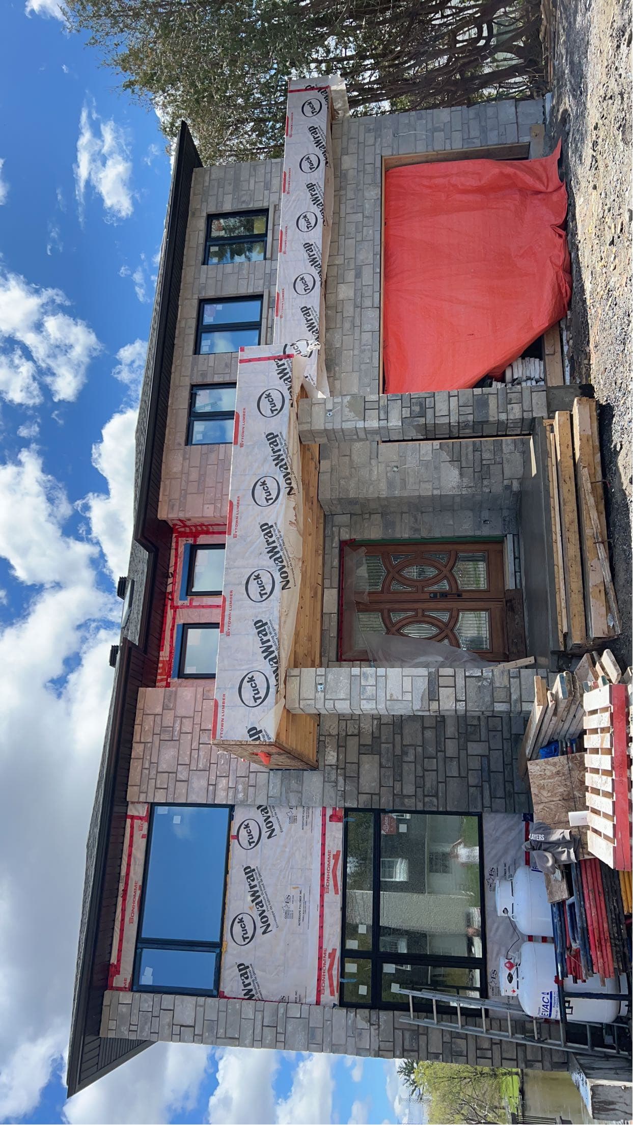 Modern grey stone house under construction with house wrap and a large orange tarp.