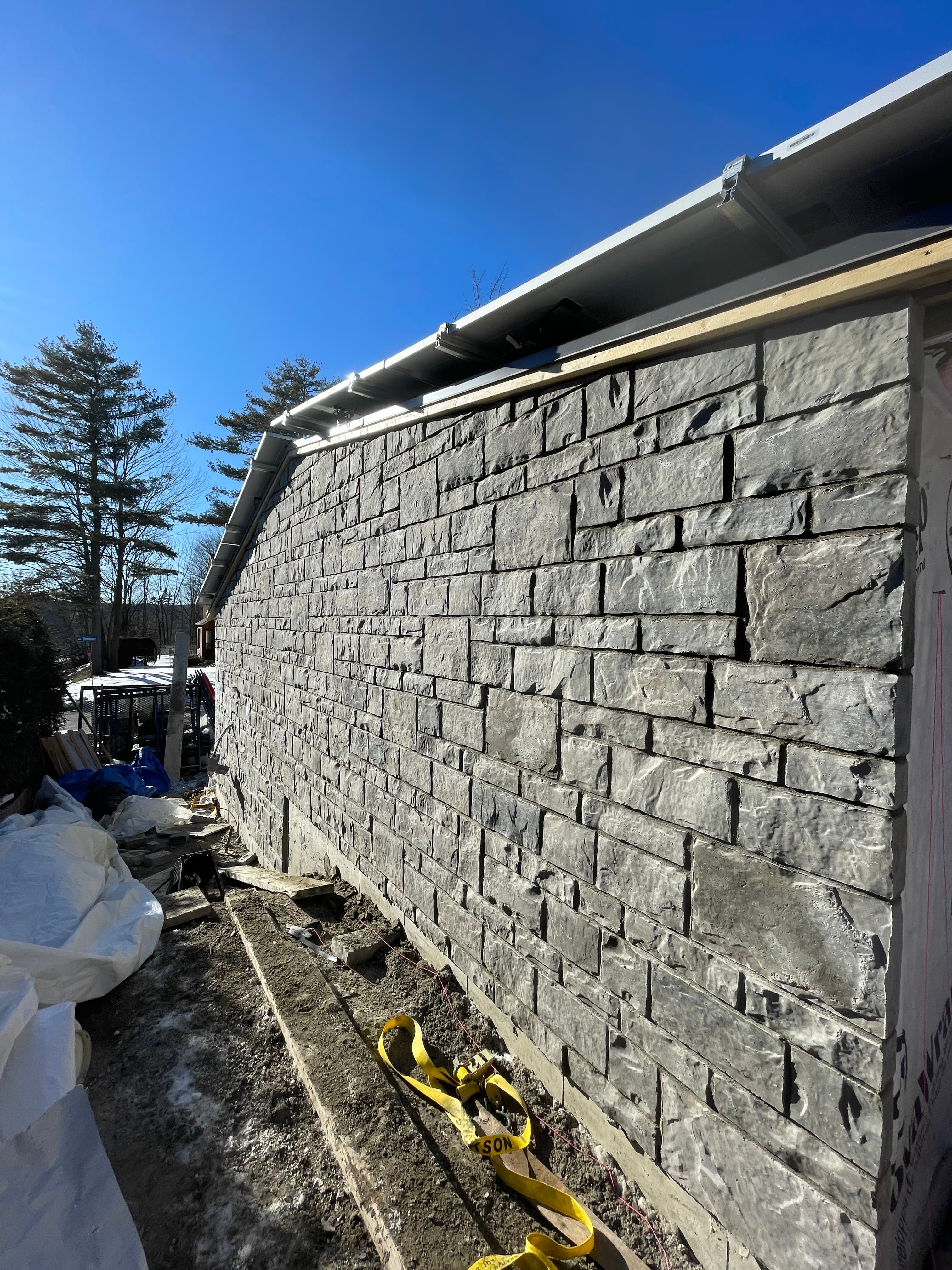 Grey rectangular stone veneer siding on a building wall under a clear blue sky.